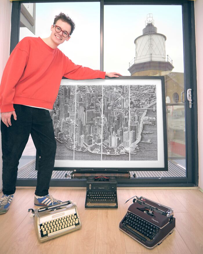 A man proudly displays a large piece of Typewriter Art of a city skyline, surrounded by vintage typewriters.
