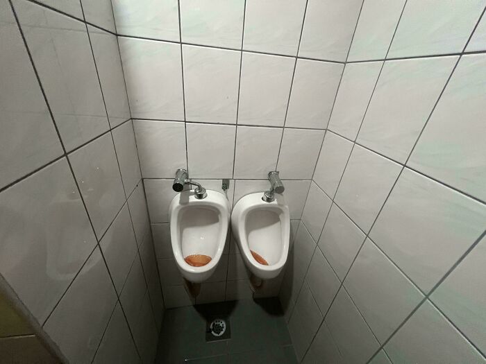 A truly bizarre sight of two urinals mounted extremely close together, almost touching, in a public restroom.