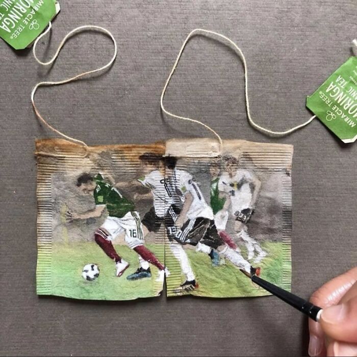 A hand painting soccer players in a miniature painting on used tea bags