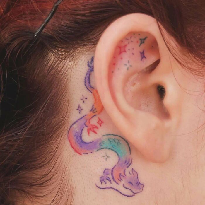 Colorful dragon tattoo behind ear with star accents