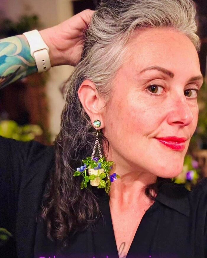 Woman wearing handmade frog-themed earrings with small purple flowers