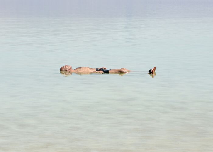Photographer creating minimalist art: a person floating on their back in serene, light-colored water.