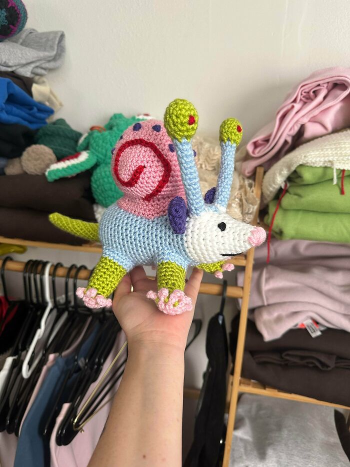 Colorful crocheted snail toy held in hand with clothing in background