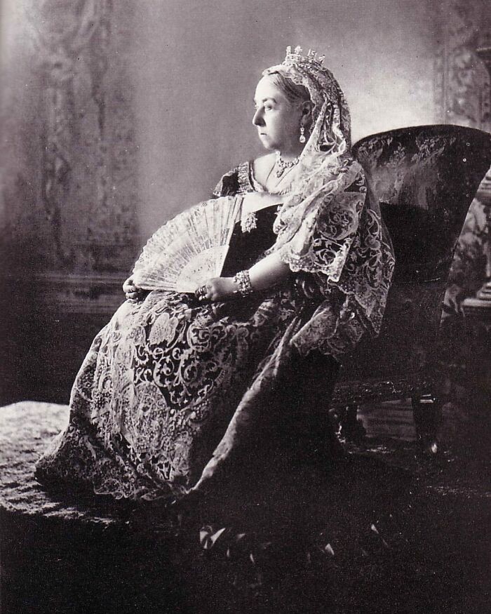 A regal black and white photo of Queen Victoria, an iconic figure among Women in History, seated with a fan, adorned in a formal gown and tiara.