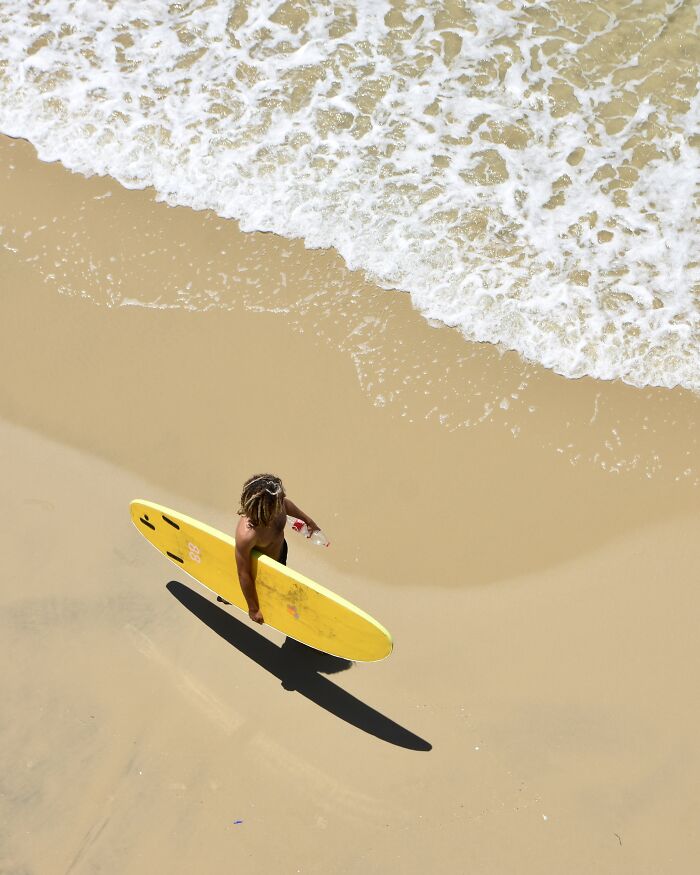 Surfer with yellow board by ocean waves on sand, a minimalist art beach scene using negative space.