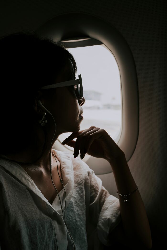 A woman with sunglasses and headphones looking out an airplane window, considering entitled people who got a reality check.