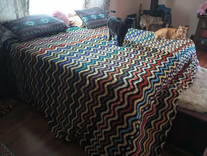 Crocheted multicolor zigzag blanket on bed with two cats