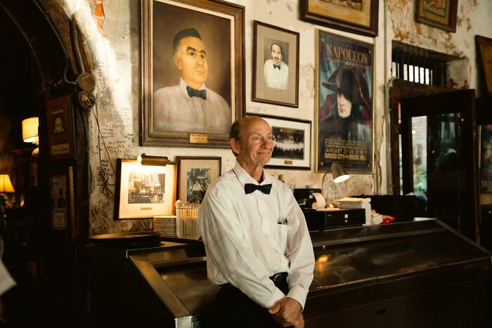 A perfectly timed street photo by Jeremy Paige, of a waiter standing in a historic room filled with portraits.