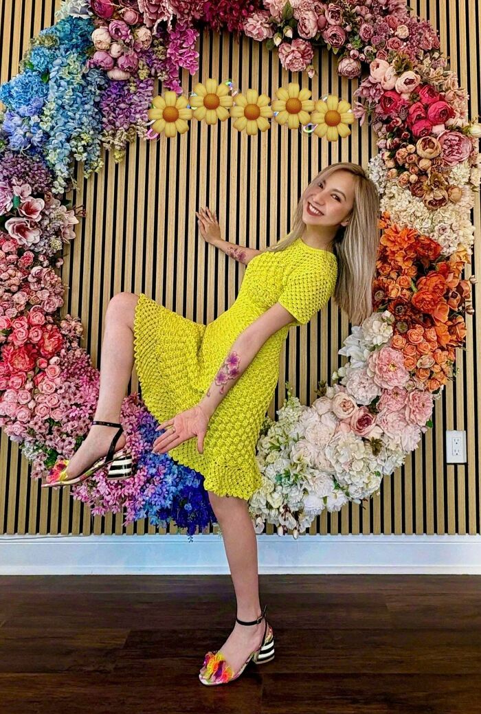 Woman in yellow crocheted dress posing by floral wall art