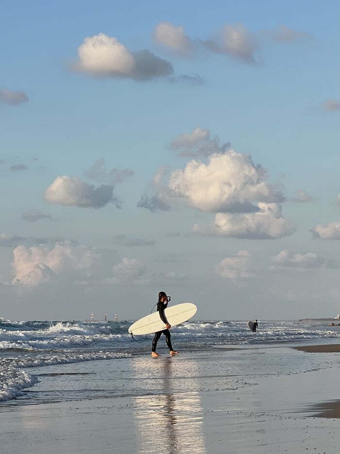 A photographer captures a surfer walking on the beach with a surfboard, showcasing minimalist art with negative space.