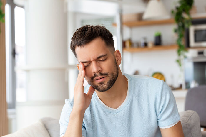 Stressed man touching temple with closed eyes in home setting
