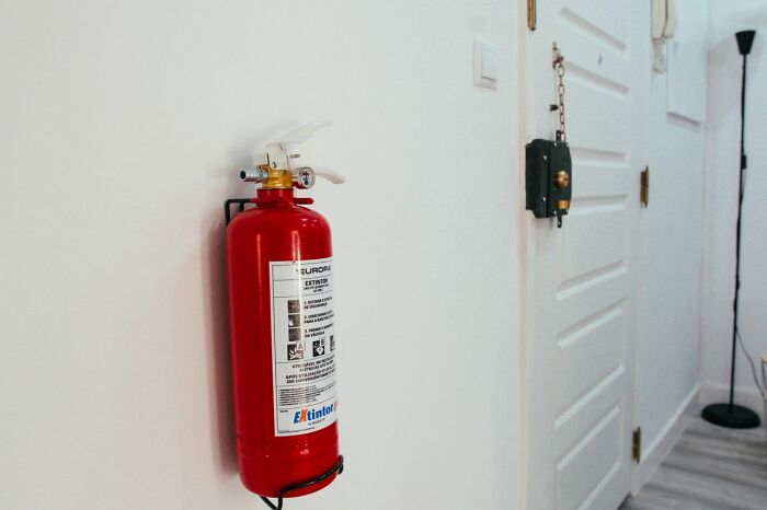 A red fire extinguisher mounted on a white wall, a safety tip for women living alone to protect themselves.