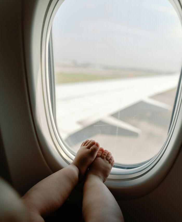 A baby's feet propped up against an airplane window, showing entitled people who got a reality check at 30,000 feet.
