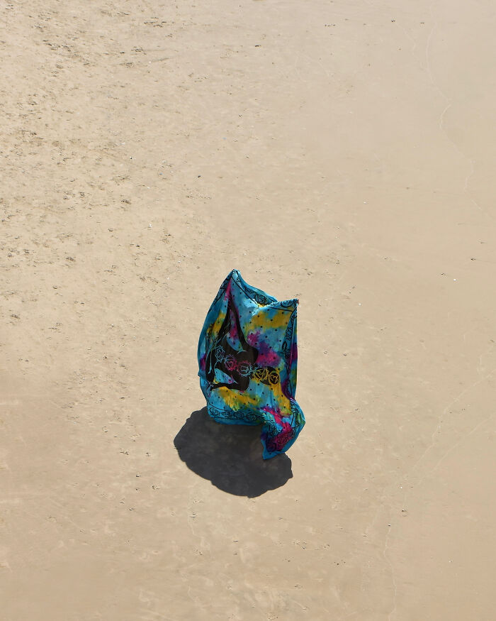 Colorful fabric on vast sand, a minimalist art beach scene using negative space by a photographer.