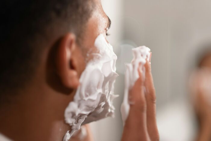 A man applying shaving cream to his face, a common grooming activity that cabin crew might deal with if requested.