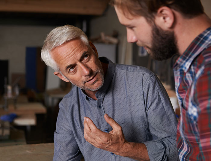 Older man giving advice in a serious conversation with a younger man indoors