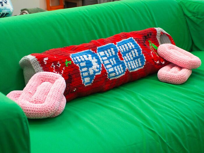 Crocheted PEZ candy-themed long pillow on green couch showing creative crochet work