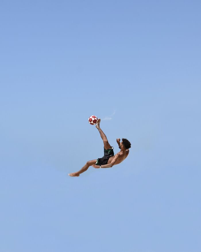 A photographer captures a person doing a bicycle kick with a football in the sky, minimalist art with negative space.