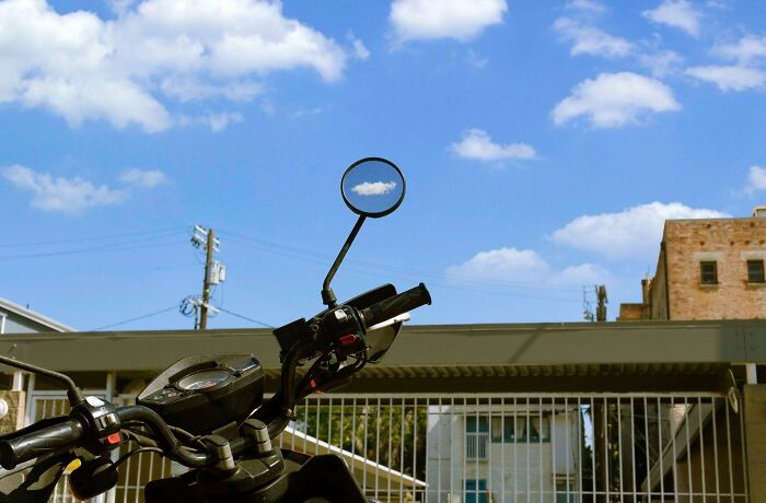 A motorcycle mirror perfectly frames a single cloud in the blue sky, a striking Jeremy Paige street photo.