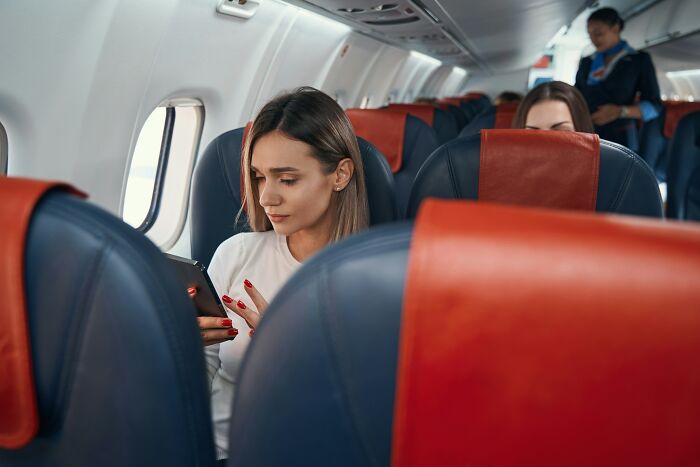 A woman looking at a tablet in an airplane, among other passengers, portraying entitled people's experiences on flights.
