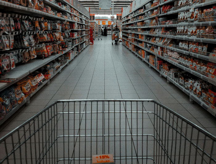 Shopping aisle with empty cart in grocery store focused on products on shelves