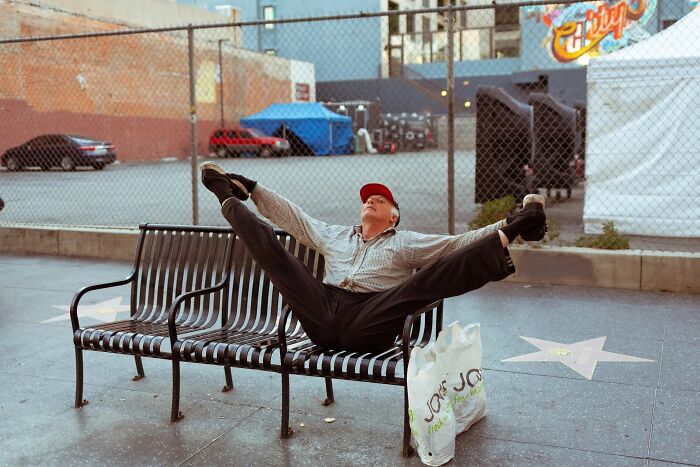 Perfectly timed street photo by Jeremy Paige of a man doing a split on a bench on the Hollywood Walk of Fame.