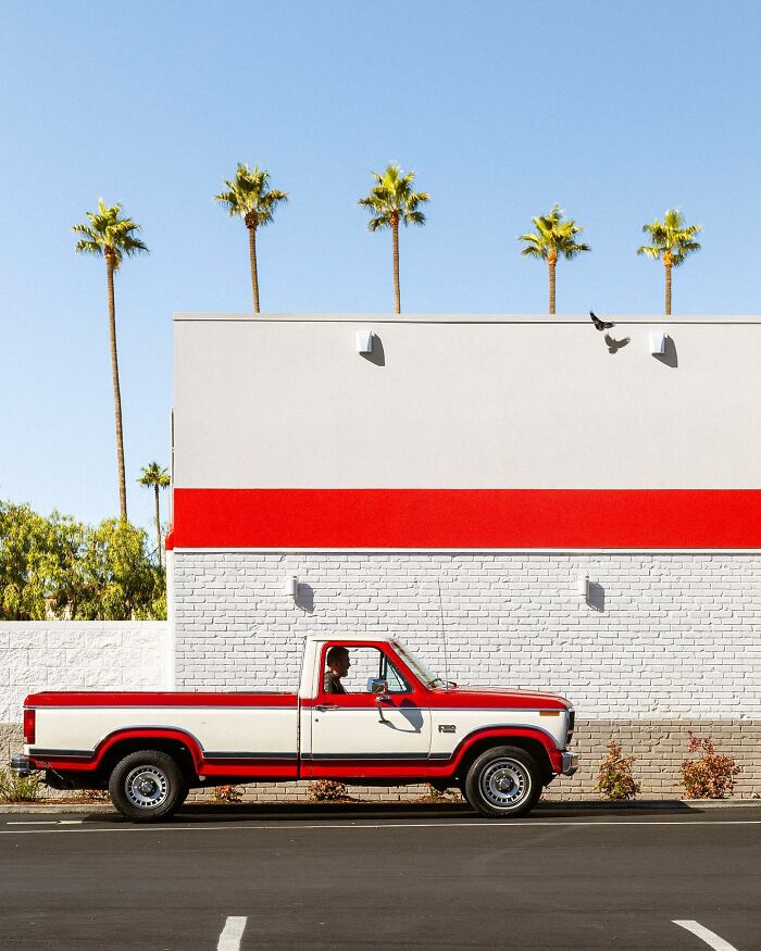 A perfectly timed street photo by Jeremy Paige of a red and white truck driving past a red and white building.