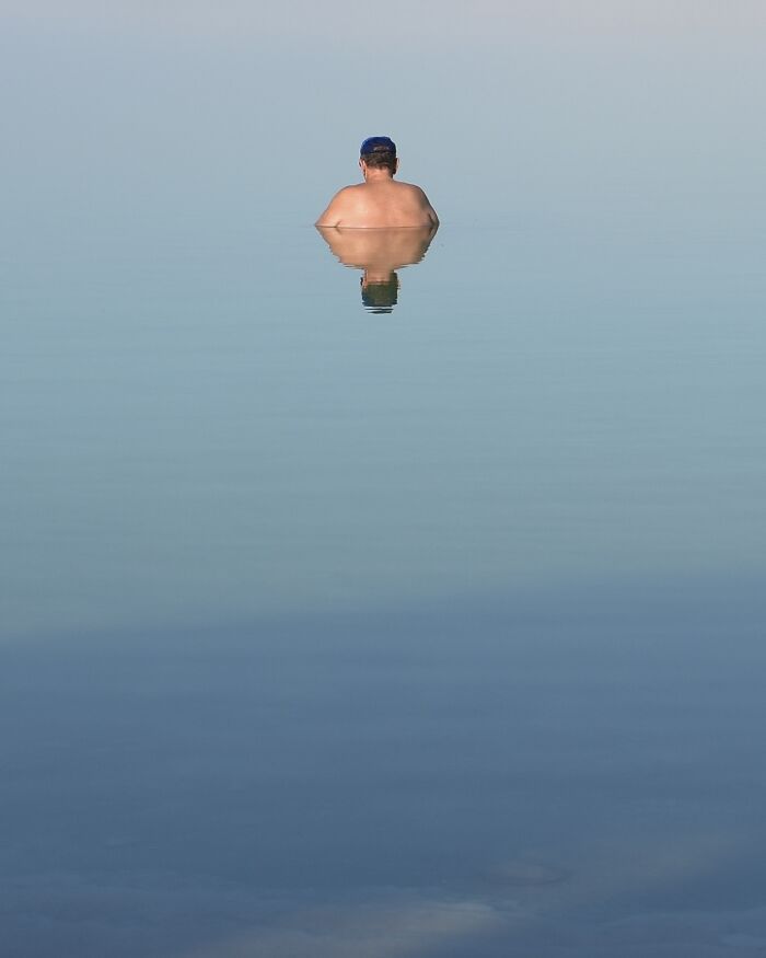 Photographer capturing minimalist art: a person with a blue cap in still water, body reflected below.