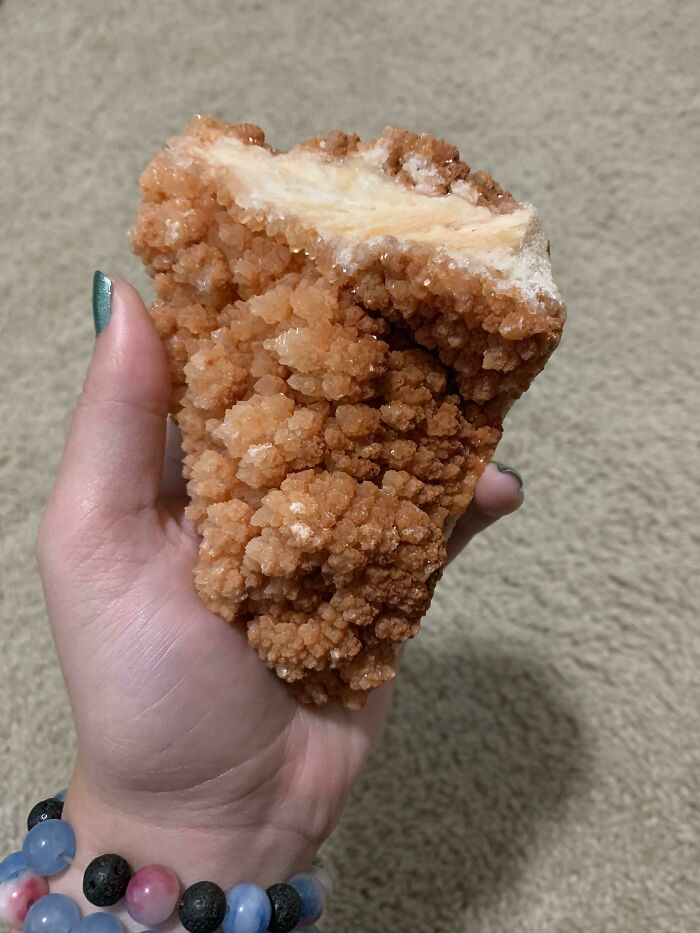 A hand holding a large, orange, crystalline rock that resembles forbidden foods.