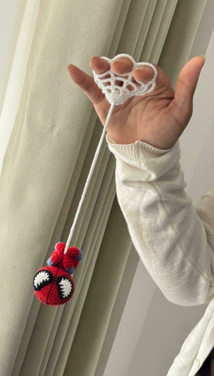 Hand holding crocheted toy spider hanging from yarn web