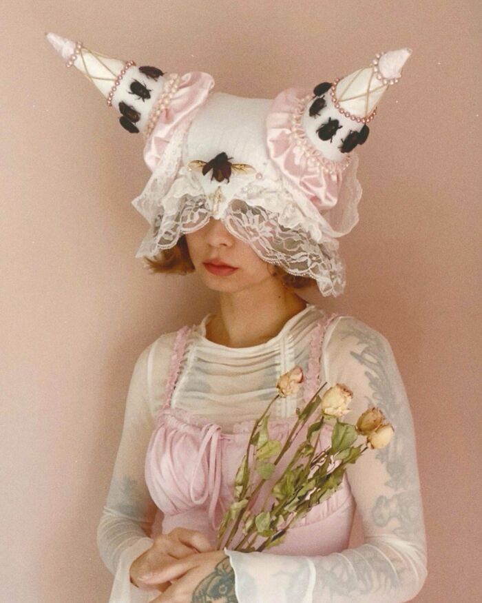 Woman wearing quirky hat with lace and bug decorations holding dried flowers