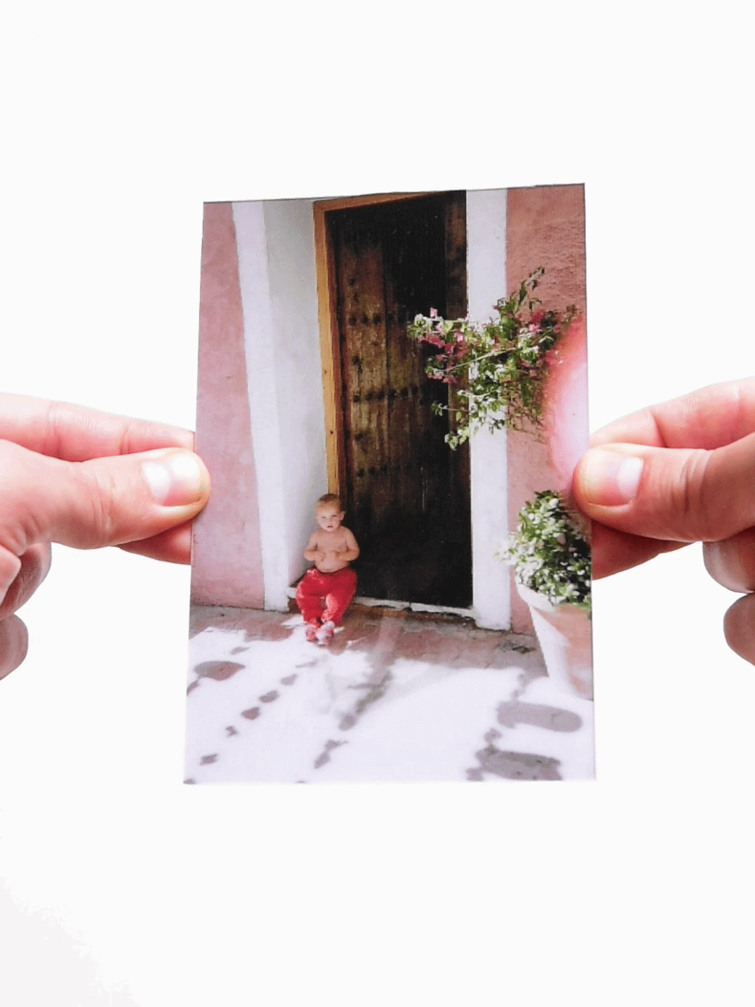 Childhood photo of a toddler sitting against a pink wall and wooden door