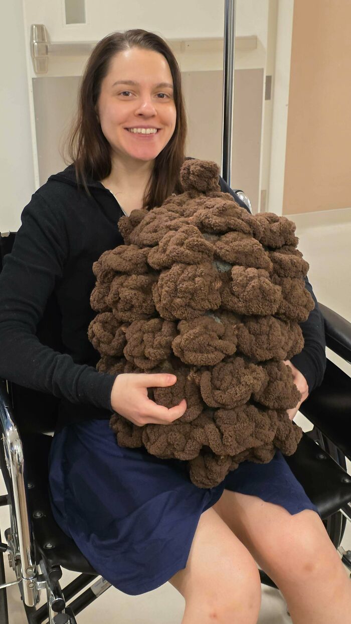 Woman holding a large chunky brown crocheted pillow sitting in wheelchair