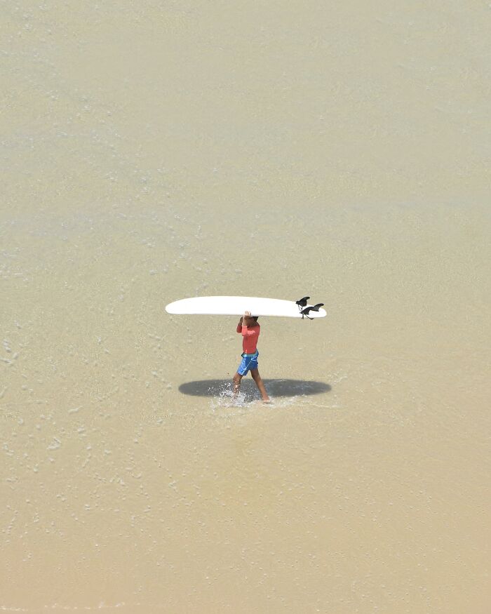 A child carries a surfboard on a wide, shallow beach, captured by a photographer as minimalist art with negative space.