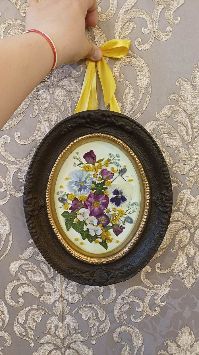 Framed pressed flower artwork with yellow ribbon hanger on patterned wallpaper
