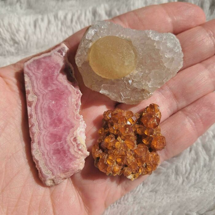 A hand holding three different types of forbidden foods, including pink and orange crystals.