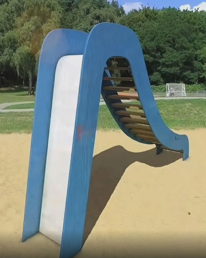 A blue and white playground slide with a steep angle and steps on the back, another instance of playground fails.