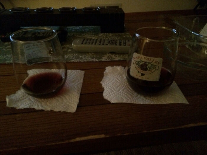 A DIY fail with two wine glasses on torn paper towel coasters on a wooden table, next to a remote control.