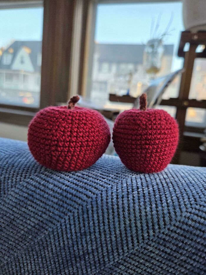 Two crocheted red apples with brown stems sitting on a blue fabric surface