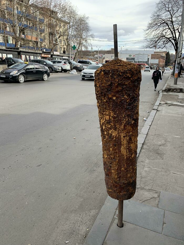 A large, rotating kebab of forbidden foods on a street in front of buildings and cars.