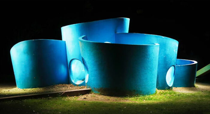 Bright blue, cylindrical structures create a surreal Japanese playground scene at night, captured by Fujio Kito.
