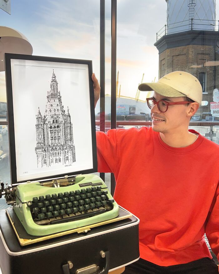A man proudly holds up a framed piece of Typewriter Art, with a vintage typewriter resting on a case nearby.