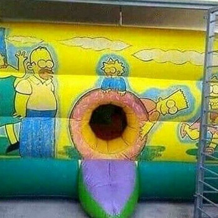 A vibrant yellow inflatable bounce house featuring Homer Simpson with a central tunnel slide, a funny playground fail.