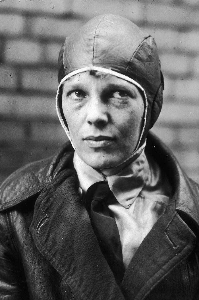 A black and white close-up of a determined woman in history wearing a flight cap and leather jacket.