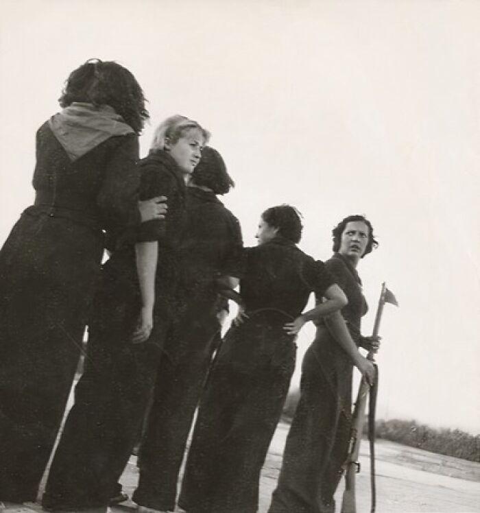 Women-In-History in dark clothes, with one holding a rifle, looking into the distance.