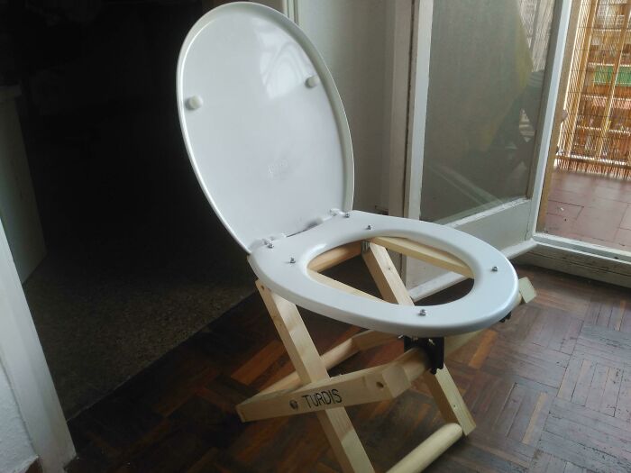 A white toilet seat attached to a wooden foldable base, showcasing a DIY fail.