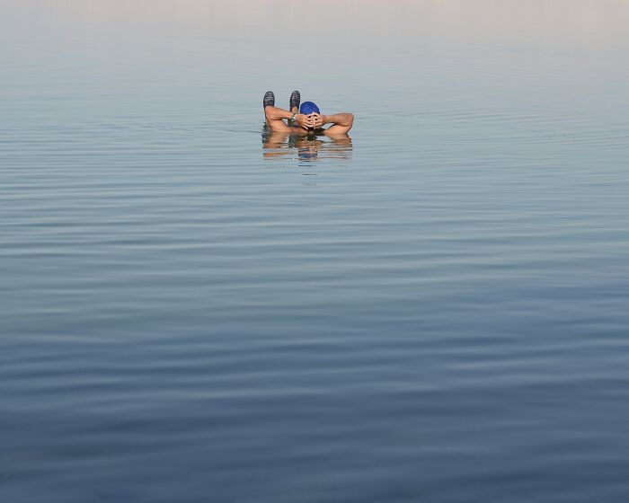 Photographer's minimalist art: a person relaxing in calm water, hands behind head, with a blue swim cap.