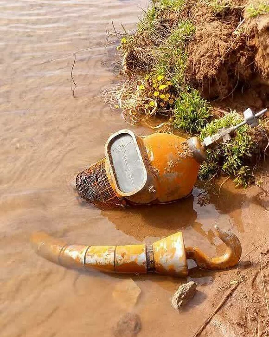 Chaotic, uncomfortable, and disturbing objects resembling a pirate's hook and a diver's helmet by the water.