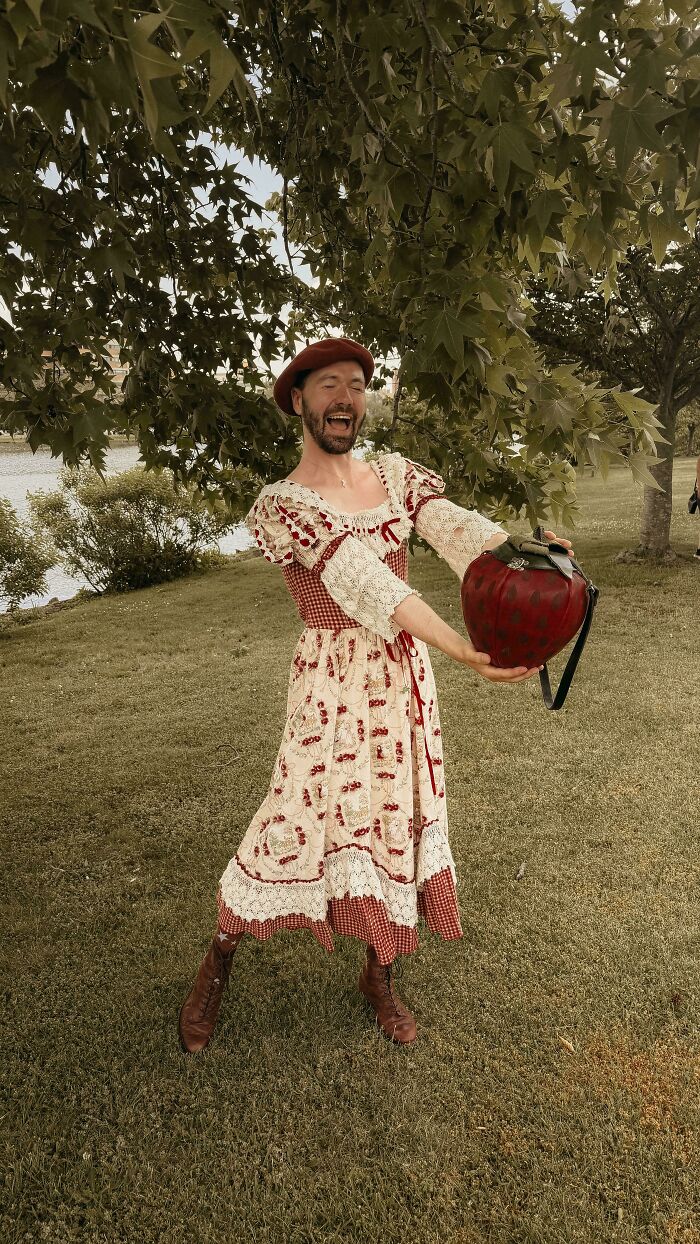 Man in vintage dress holding quirky frog bag outside under tree