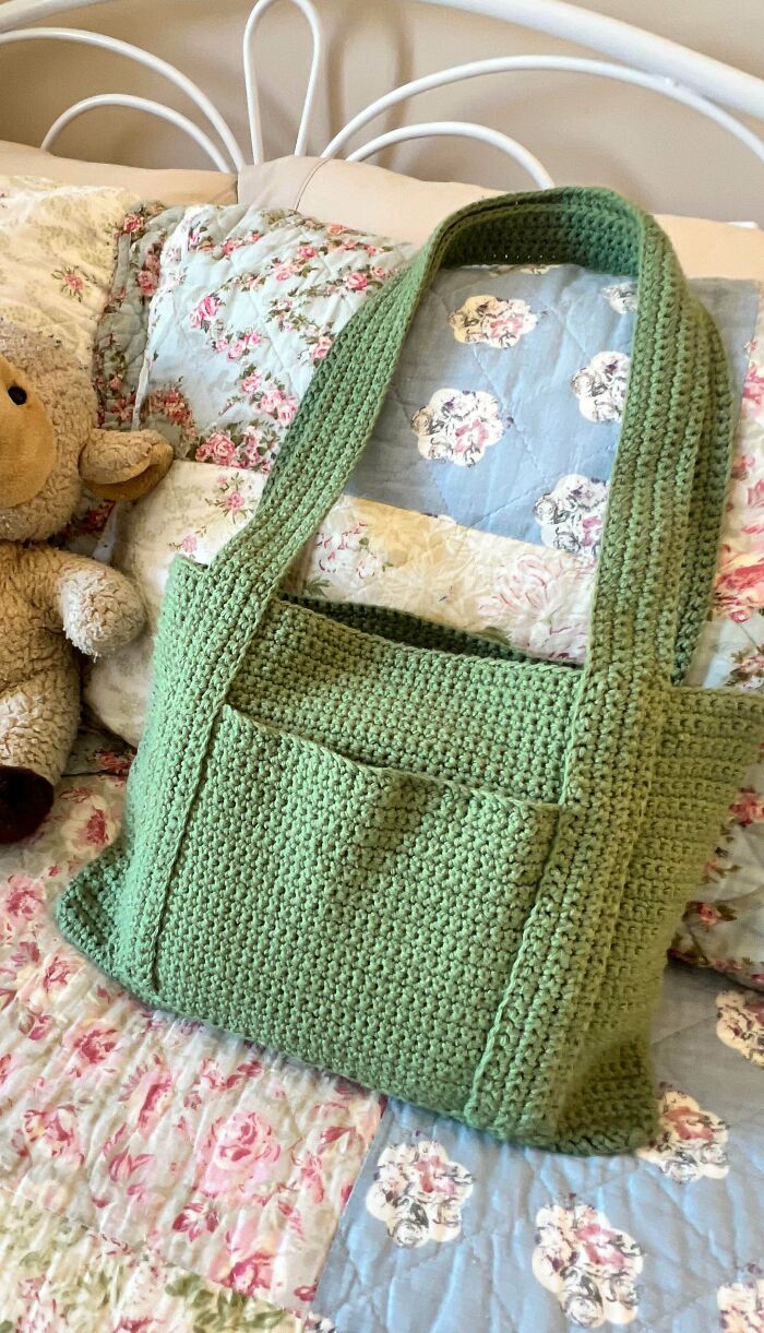 Green crocheted handbag with long strap on floral quilted bedspread